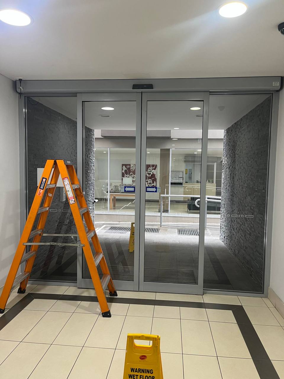 NEWGEN technician servicing an automatic sliding door system inside a commercial building — full inspection and adjustment in progress